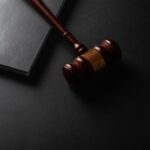 A wooden gavel resting on a dark surface next to a closed notebook
