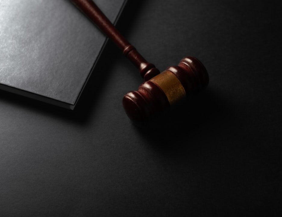 A wooden gavel resting on a dark surface next to a closed notebook
